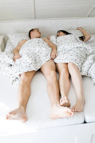 Beine von Mann und Frau auf weißem Bettlaken teilweise bedeckt. — Stockfoto