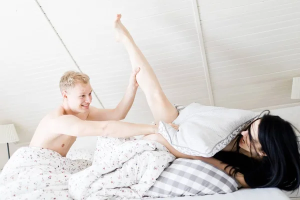 Casal jovem que tem a guerra de travesseiro no quarto de sótão - perna para cima — Fotografia de Stock
