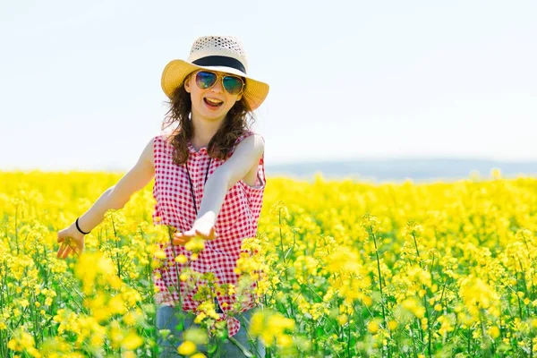 Chica joven en vestido rojo a cuadros y sombrero de sol posando en campo de colza oleaginosa —  Fotos de Stock