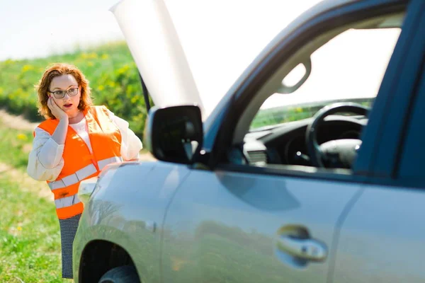 Une femme en gilet orange capot de voiture ouvert de voiture cassée — Photo