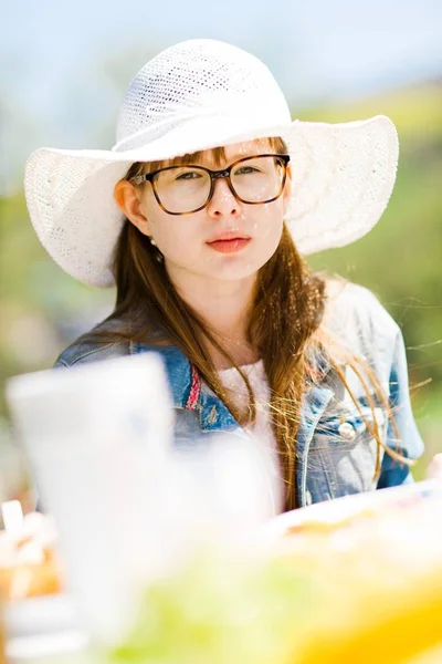 Adolescente envejecida chica en blanco sunhat sentado por mesa en cumpleaños gard —  Fotos de Stock