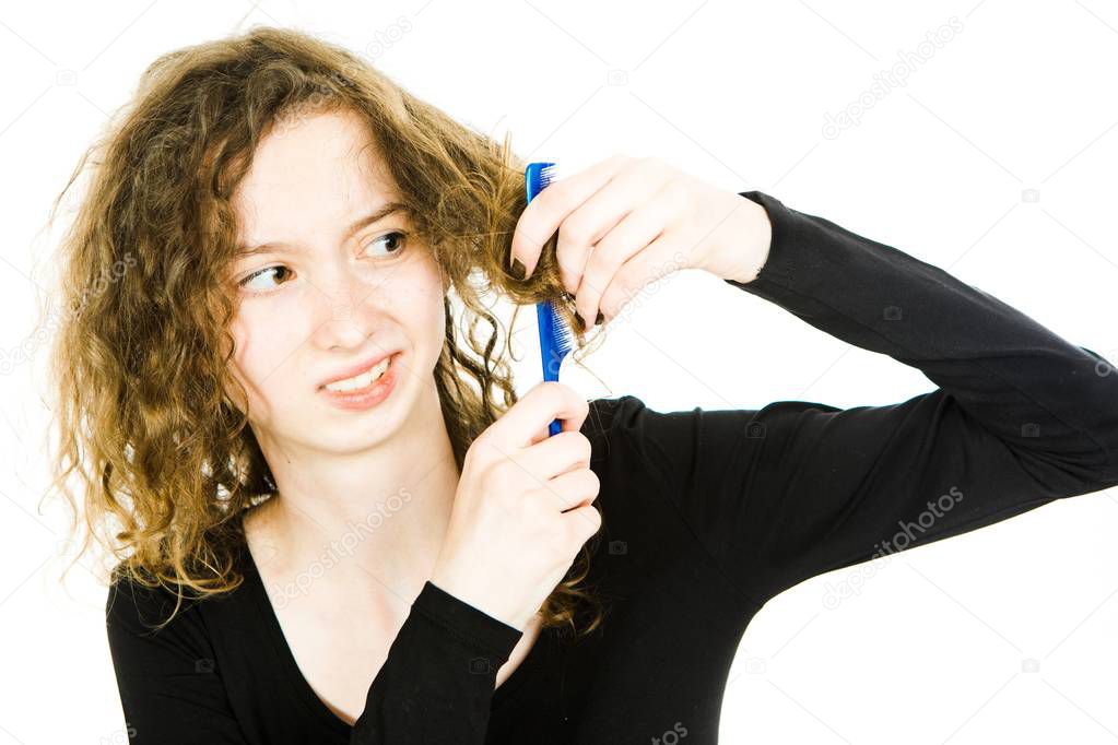 Teenaged blond girl with hair having tangled hair dressing problem - combing curly hair.