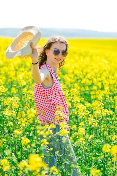 Chica joven en vestido rojo a cuadros y sombrero de sol posando en campo de colza oleaginosa . —  Fotos de Stock