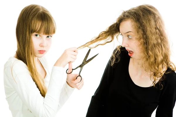 Δύο κορίτσια με ξανθά μαλλιά και ψαλίδι, το ένα θα κόψει τις τρίχες για να κάνει καλύτερο κούρεμα, δεύτερο με σγουρά μαλλιά προσπαθούν να αποφύγουν. — Φωτογραφία Αρχείου