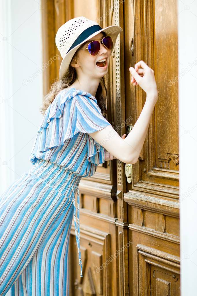 Teenaged girl in jumpsuit dress is knocking on vintage door.