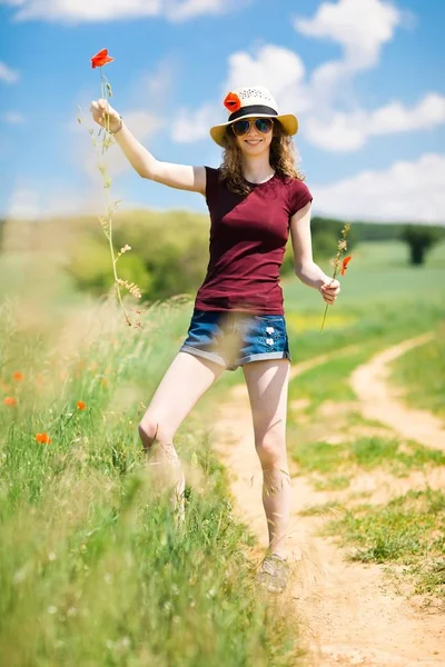 Una joven con sombrero arranca una flor de amapola con raíces . —  Fotos de Stock