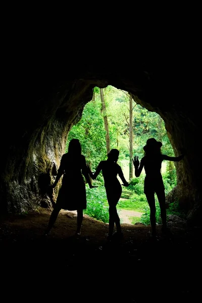 Dark female silhouettes at the entrance to natural cave in the forrest.