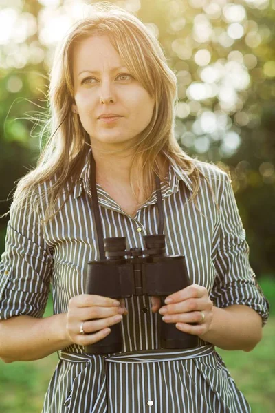 A female tourist explorer with binoculars stays outdoor.