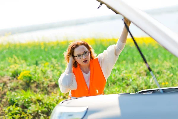 Een vrouw in oranje vest open auto motorkap van gebroken auto — Stockfoto