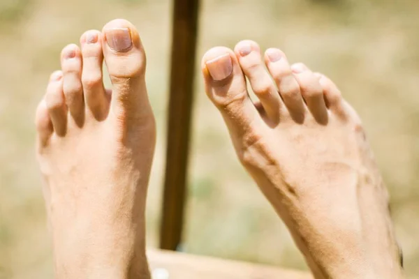 Woman\'s foot on wooden chair outdoor.