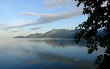 sessiz yüzeyinde göl İşkodra arka plan dağlar ve gökyüzü bulutlu