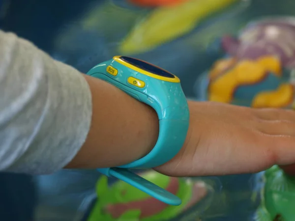 Children's smart watch of blue color on a hand of the girl against a background of toys floating in water