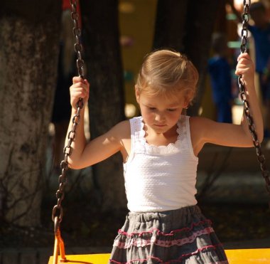 beyaz t-shirt ve gri etek küçük kız bir yaz günü bir şehir parkında bir salıncak üzerinde oturur