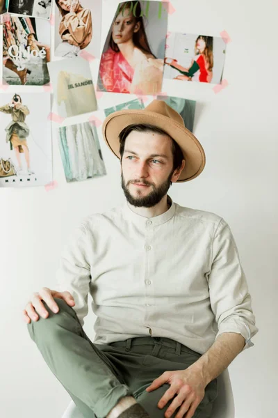 Stylish handsome man in a hat sitting on chair near white wall