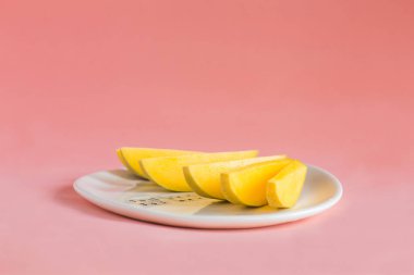 Mango dilimleri pembe bir arka plan üzerinde beyaz plaka