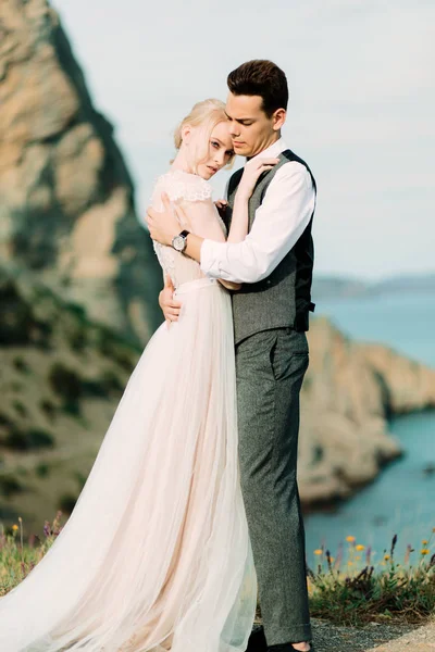 Impresionante novia y el novio se abrazan tiernos de pie en la colina dorada —  Fotos de Stock