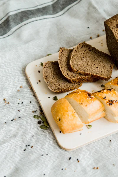 在灰色布上的木板上吃新鲜切片面包 — 图库照片