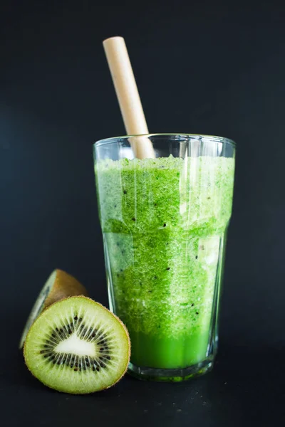 Healthy green smoothie in a glass cup on a black background