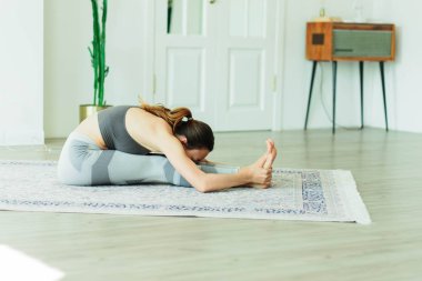 Parlak bir odada yoga yapan çekici, gülümseyen bir kadın.