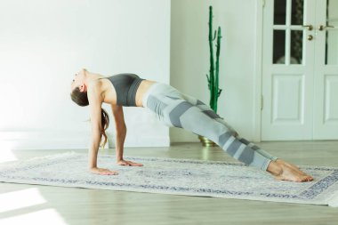 Parlak bir odada yoga yapan çekici, gülümseyen bir kadın.