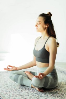 Parlak bir odada yoga yapan çekici, gülümseyen bir kadın.