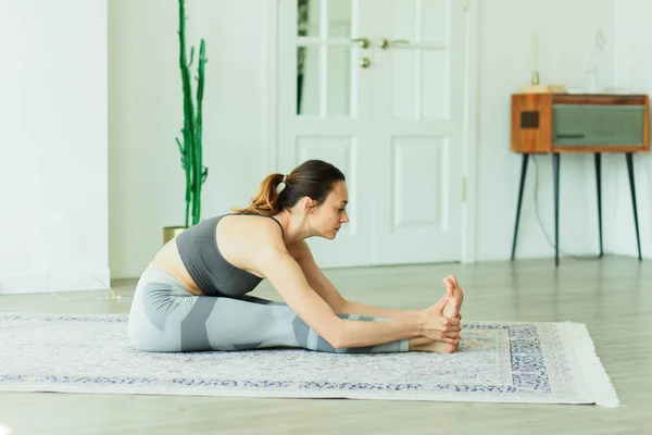 Parlak bir odada yoga yapan çekici, gülümseyen bir kadın.