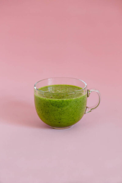 Healthy green smoothie in a glass cup on pink background
