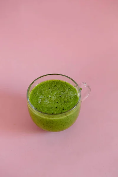 Healthy green smoothie in a glass cup on pink background