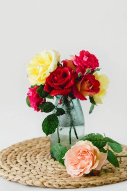 Beyaz arka planda bir hasır peçete üzerinde vazo coloful güller