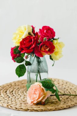 Beyaz arka planda bir hasır peçete üzerinde vazo coloful güller