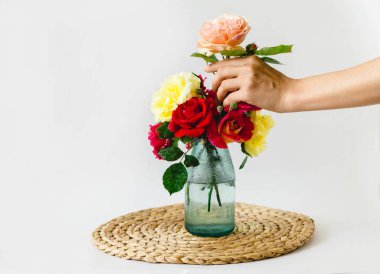 beyaz bir arka planda bir hasır peçete üzerinde bir vazo renkli gül bileşimi