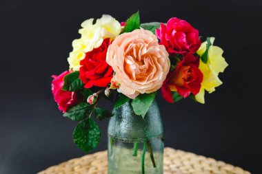 Siyah arka planda bir hasır peçete üzerinde vazo coloful güller