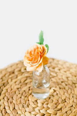 Turuncu beyaz arka planda bir hasır peçete üzerinde cam vazo yükseldi