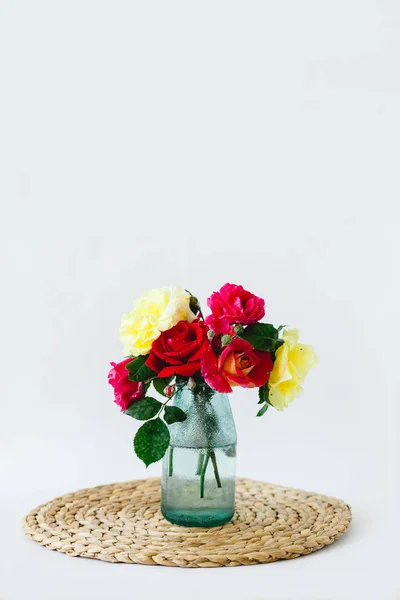 Beyaz bir arka planda bir hasır peçete üzerinde bir vazo renkli gül bileşimi — Stok fotoğraf