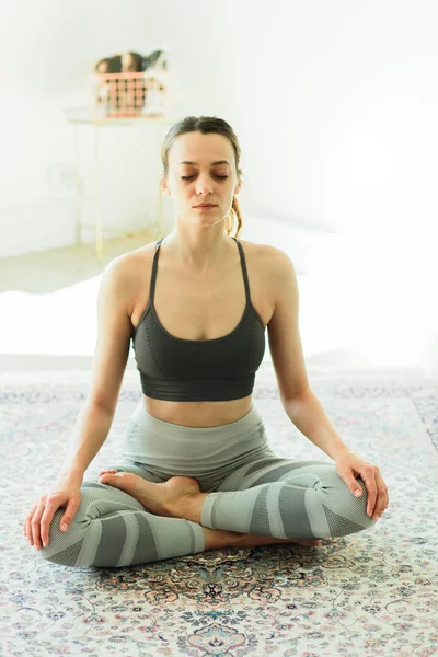 Молодая симпатичная улыбчивая женщина практикует йогу в светлой комнате — стоковое фото