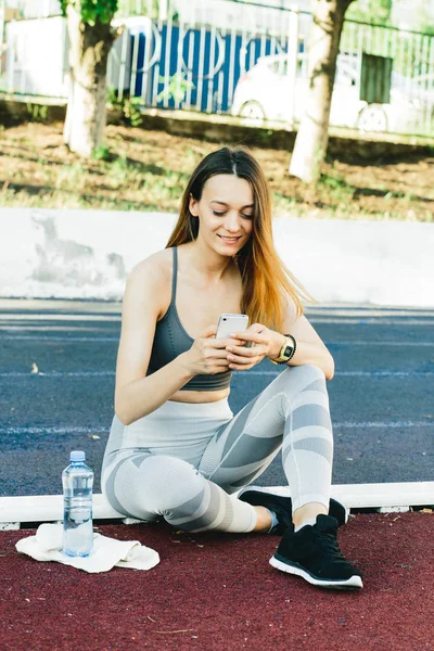 Young woman sitting on the ground with a bottle of water after Jogging outdoors