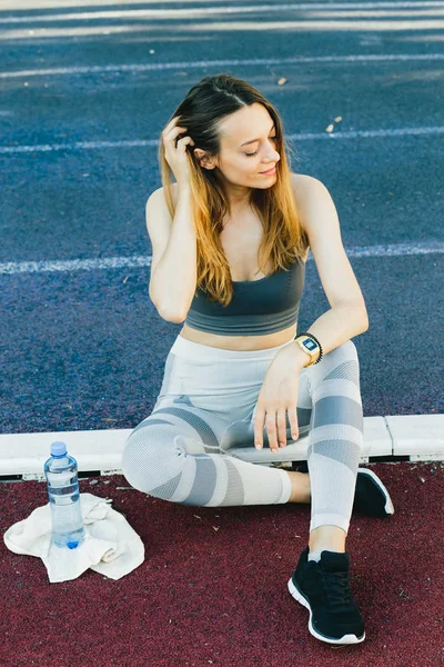 Jovem mulher sentada no chão com uma garrafa de água depois de correr ao ar livre — Fotografia de Stock