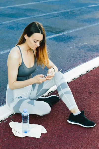 Jovem mulher sentada no chão com uma garrafa de água depois de correr ao ar livre — Fotografia de Stock