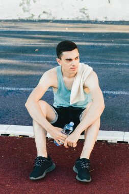 Dışarıda koşu yaptıktan sonra bir şişe suyla yerde oturan genç adam