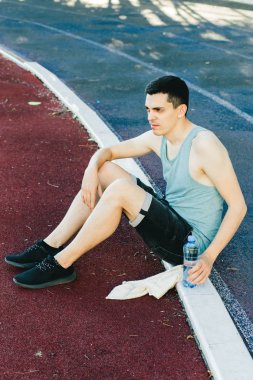 Dışarıda koşu yaptıktan sonra bir şişe suyla yerde oturan genç adam