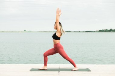 göl kenarında iskelede açık havada yoga yapan genç kız.