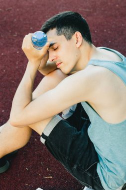 Dışarıda koşu yaptıktan sonra bir şişe suyla yerde oturan genç adam