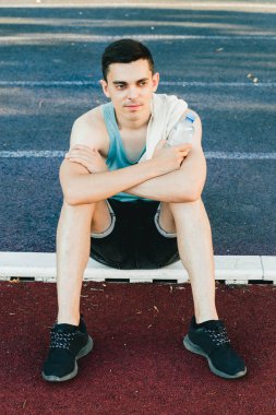 Dışarıda koşu yaptıktan sonra bir şişe suyla yerde oturan genç adam