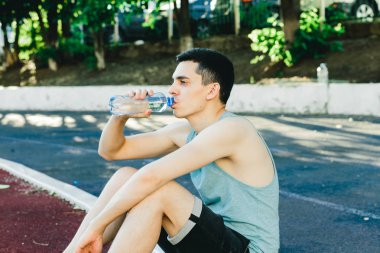 Dışarıda koşu yaptıktan sonra bir şişe suyla yerde oturan genç adam