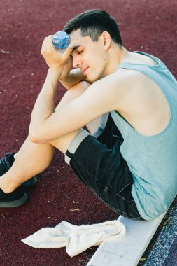 Dışarıda koşu yaptıktan sonra bir şişe suyla yerde oturan genç adam