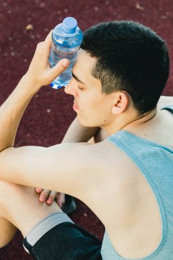 Dışarıda koşu yaptıktan sonra bir şişe suyla yerde oturan genç adam