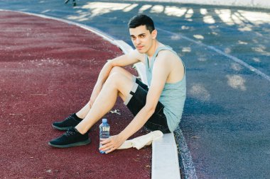 Dışarıda koşu yaptıktan sonra bir şişe suyla yerde oturan genç adam