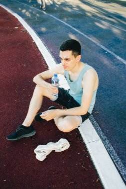 Dışarıda koşu yaptıktan sonra bir şişe suyla yerde oturan genç adam