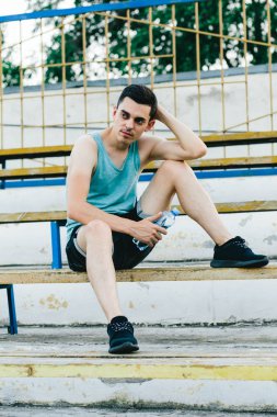 Bir bankta oturan ve ayakkabı bağcıklarını temiz havaya bağlayan genç bir adam.