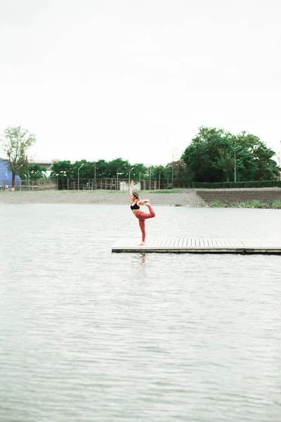 Asyalı genç kız göl kenarında iskelede açık havada yoga yapıyor. — Stok fotoğraf